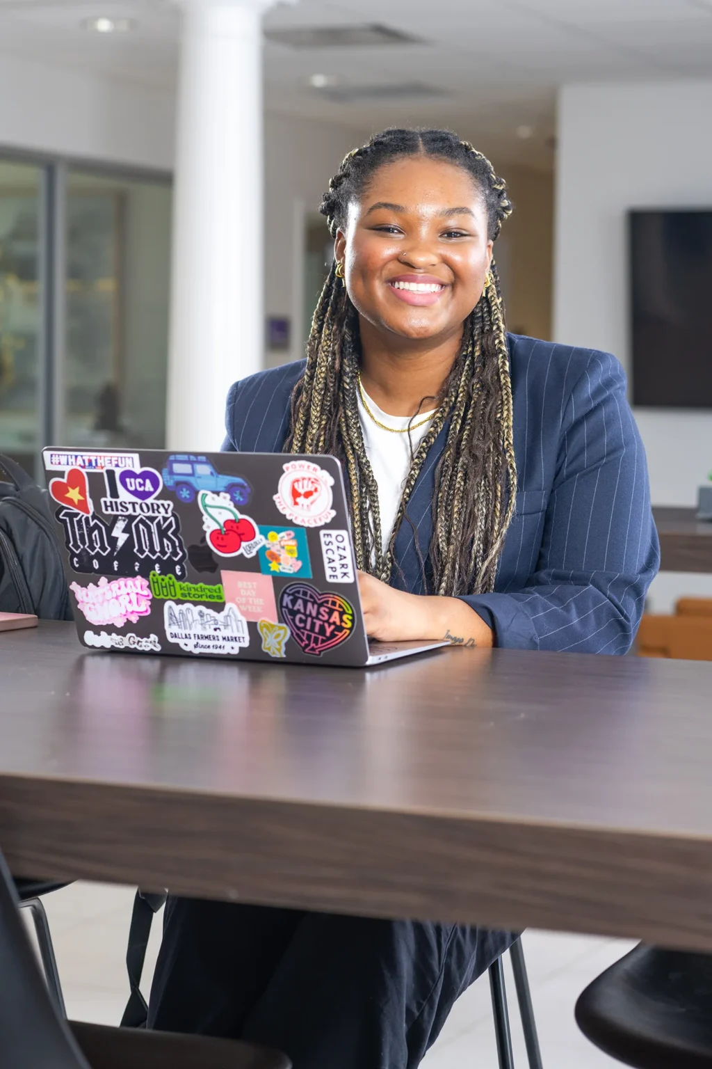Student smiling at the camera while working on a laptop covered in stickers